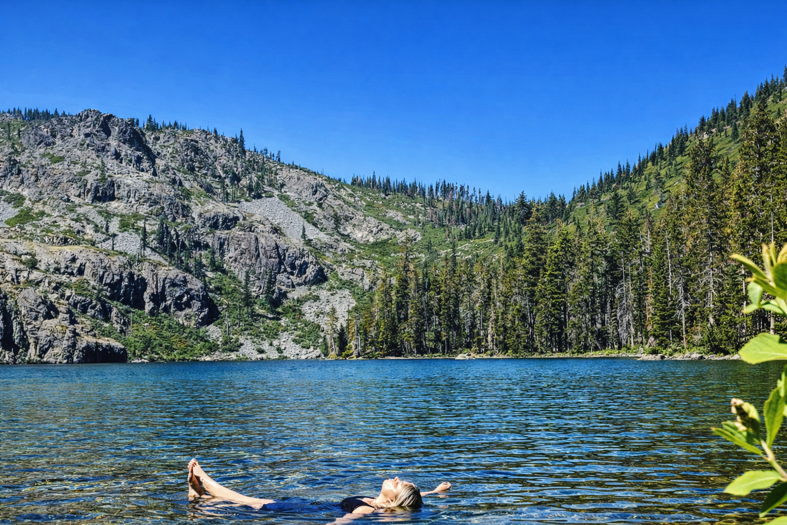Person swimming in a lake with mountains and trees in the background